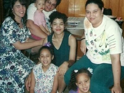 Sandra Griner is sitting on a chair with Brittney Griner resting her head in her leg as she is surrounded by her family.